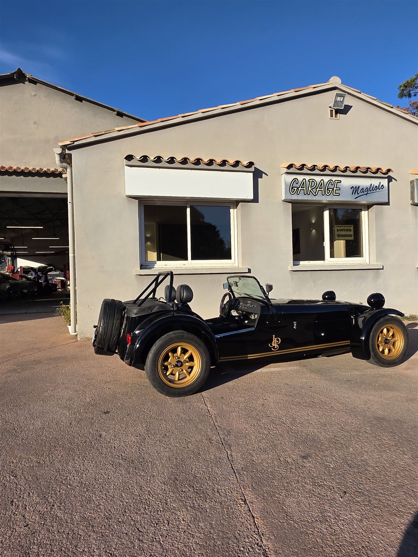 Caterham Seven noire et or devant l'enseigne du Garage Magliolo à Porto-Vecchio