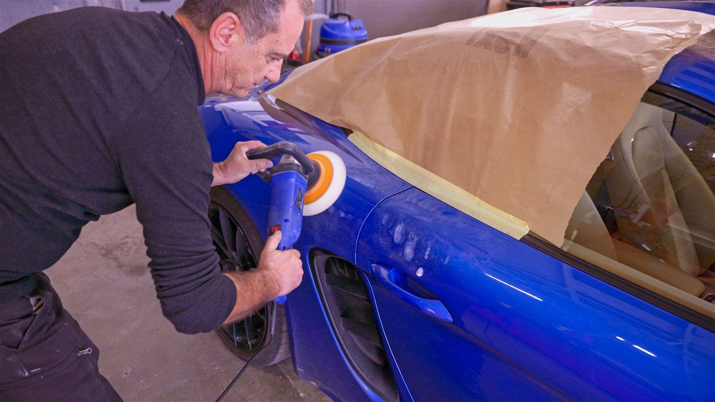 Lustrage à la polisseuse d'une Porsche bleue dans l'atelier