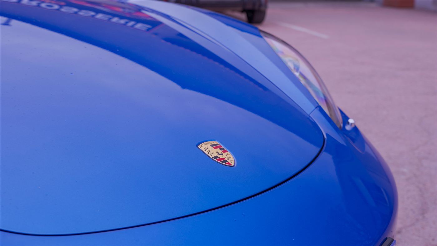 Capot d'une Porsche bleue à la peinture éclatante devant la Carrosserie Magliolo