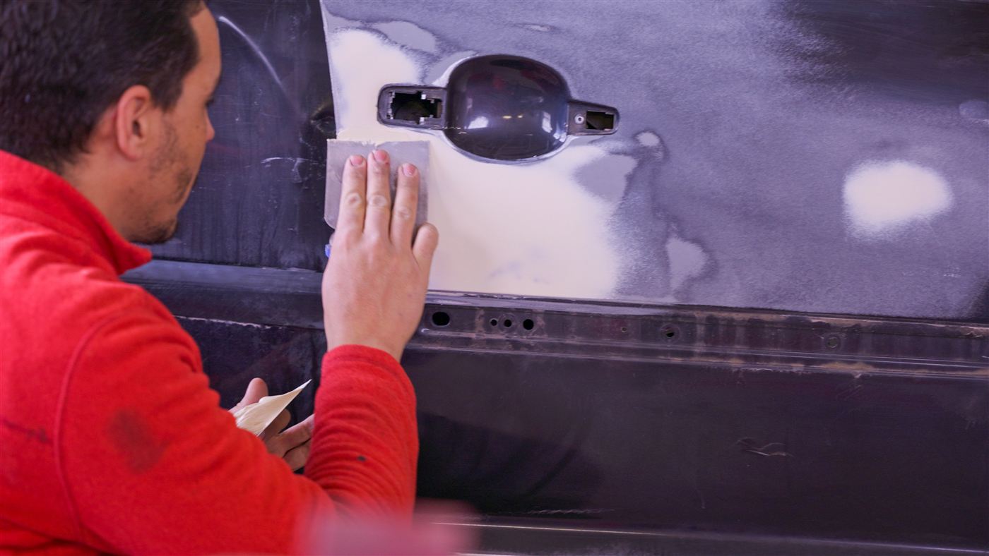 Hicham prépare une portière au masticage dans l'atelier de carrosserie